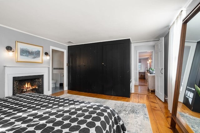 bedroom with crown molding, ensuite bathroom, and light wood-type flooring