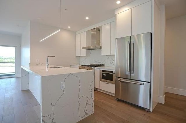 60 Newbury St Unit 10, Quincy, MA 02171 - kitchen with high quality appliances, wall chimney exhaust hood, a sink, light wood-type flooring, and white cabinetry
