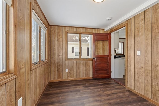 empty room featuring dark wood finished floors, wood walls, and baseboards