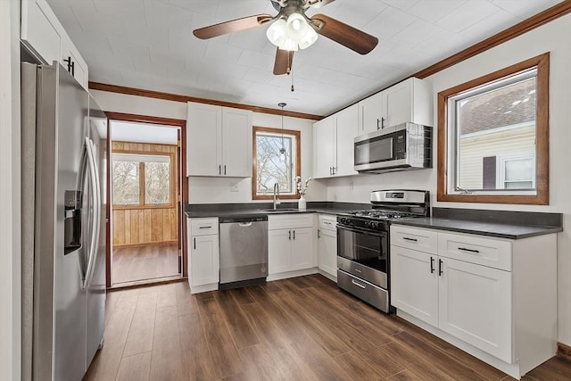 kitchen with stainless steel appliances, a sink, white cabinetry, dark countertops, and dark wood finished floors