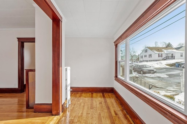 hall featuring a residential view, baseboards, crown molding, and light wood finished floors