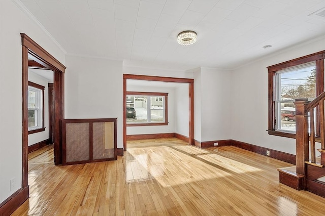 empty room with stairs, ornamental molding, light wood-type flooring, and baseboards