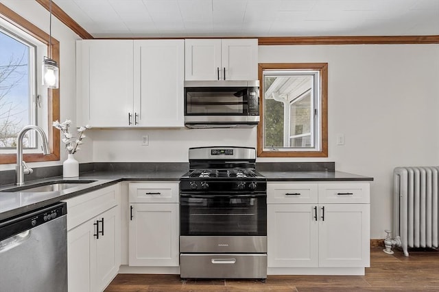 kitchen with stainless steel appliances, a sink, white cabinets, radiator heating unit, and dark countertops