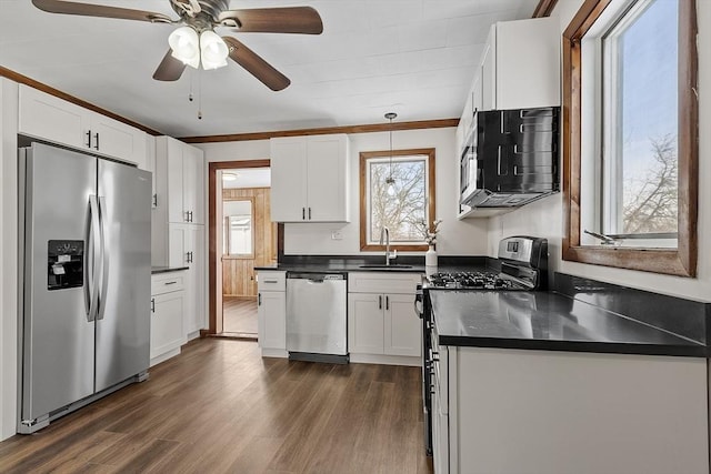 kitchen featuring stainless steel appliances, a sink, white cabinets, dark countertops, and pendant lighting