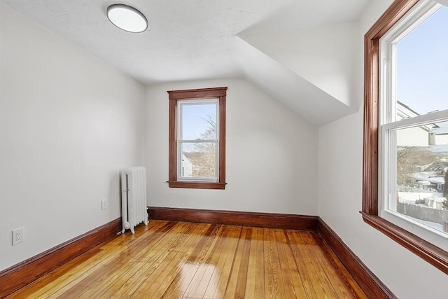 additional living space with vaulted ceiling, radiator heating unit, baseboards, and light wood-style floors