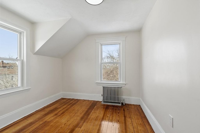 additional living space featuring radiator, vaulted ceiling, wood-type flooring, and baseboards