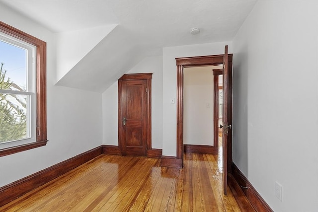 additional living space featuring baseboards, a healthy amount of sunlight, vaulted ceiling, and hardwood / wood-style floors