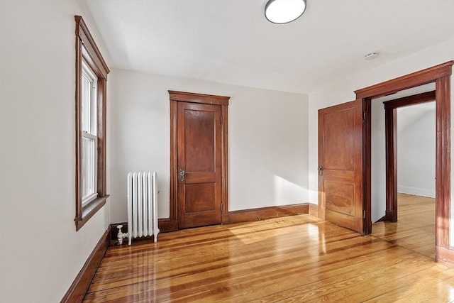 spare room with baseboards, wood-type flooring, and radiator