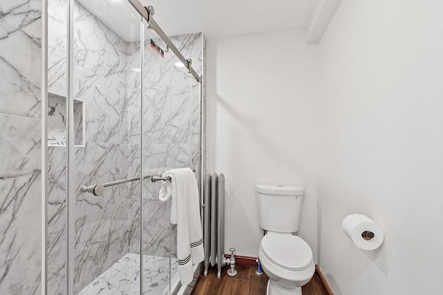 bathroom with a marble finish shower, radiator heating unit, toilet, wood finished floors, and baseboards