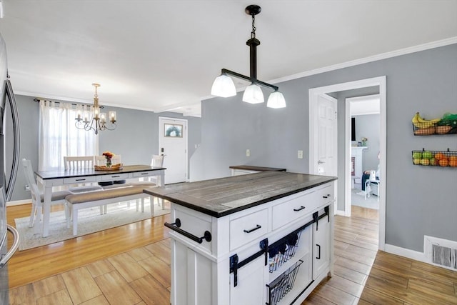 kitchen with crown molding, a kitchen island, pendant lighting, and white cabinets