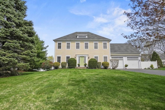 colonial-style house with fence, an attached garage, driveway, and a front lawn