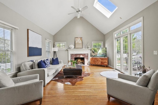 living area featuring ceiling fan, a fireplace, high vaulted ceiling, wood finished floors, and a skylight
