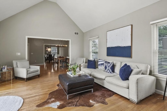living room featuring visible vents, baseboards, high vaulted ceiling, light wood-type flooring, and a chandelier