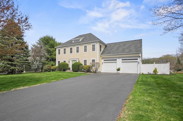 colonial inspired home featuring fence, roof with shingles, a front lawn, a garage, and driveway