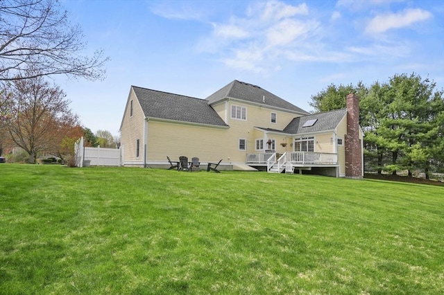rear view of house featuring fence, a wooden deck, a chimney, and a yard