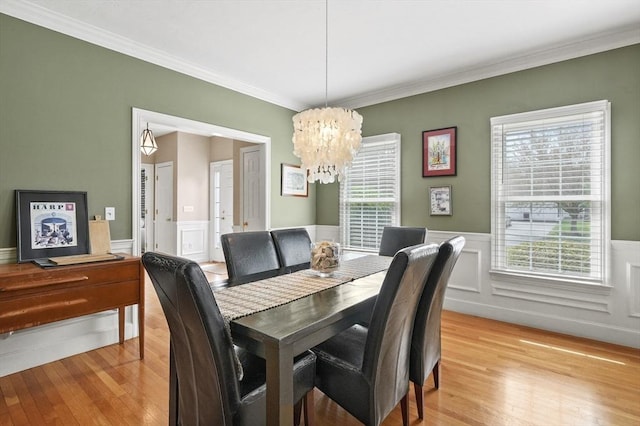 dining room featuring wainscoting, a chandelier, ornamental molding, and light wood-style floors