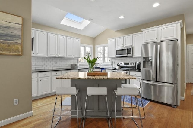 kitchen with white cabinetry, appliances with stainless steel finishes, decorative backsplash, and lofted ceiling with skylight