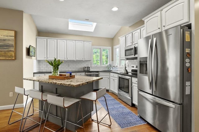 kitchen featuring appliances with stainless steel finishes, a kitchen breakfast bar, wood finished floors, and white cabinetry