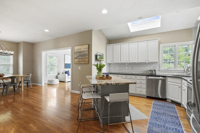 kitchen with a sink, plenty of natural light, white cabinetry, stainless steel dishwasher, and a skylight