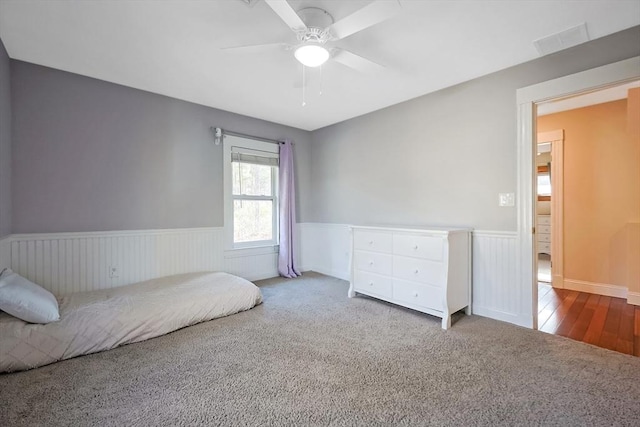 unfurnished bedroom with carpet flooring, a ceiling fan, visible vents, and wainscoting