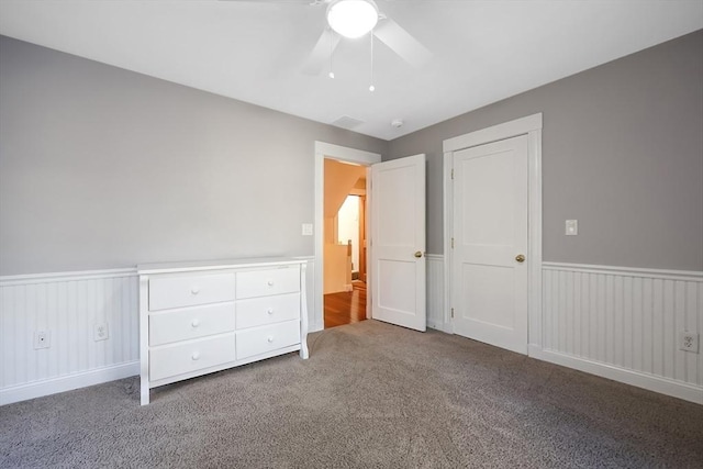 unfurnished bedroom with a ceiling fan, visible vents, carpet floors, and wainscoting