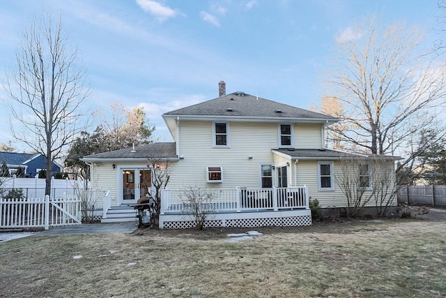 rear view of house featuring fence, a yard, a shingled roof, a wooden deck, and a chimney