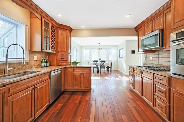 kitchen with glass insert cabinets, brown cabinetry, appliances with stainless steel finishes, and a sink