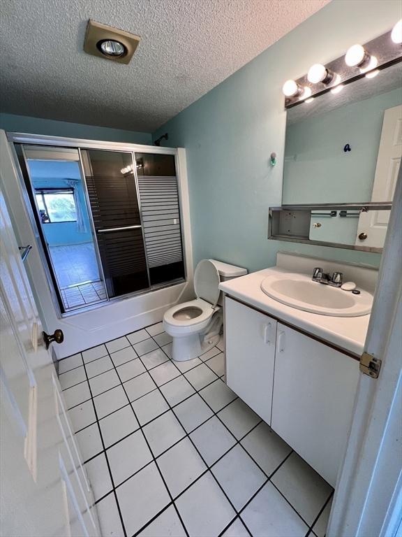 full bathroom with vanity, tile patterned floors, toilet, enclosed tub / shower combo, and a textured ceiling