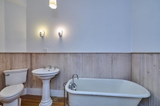 bathroom featuring wainscoting, toilet, a freestanding bath, wooden walls, and wood finished floors