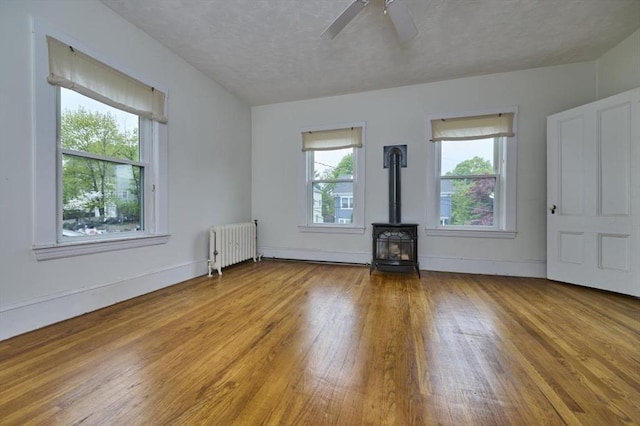 unfurnished living room with radiator heating unit, wood finished floors, a wood stove, a textured ceiling, and a ceiling fan