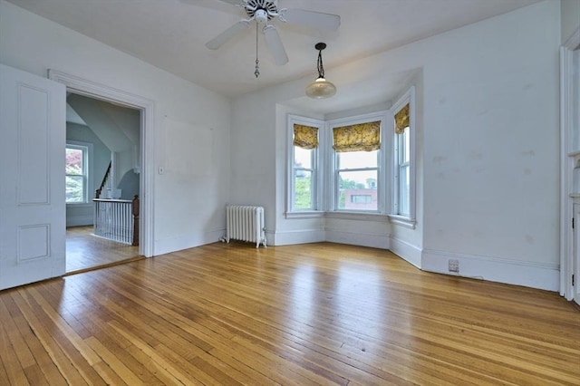 unfurnished room with radiator, light wood-type flooring, ceiling fan, and baseboards