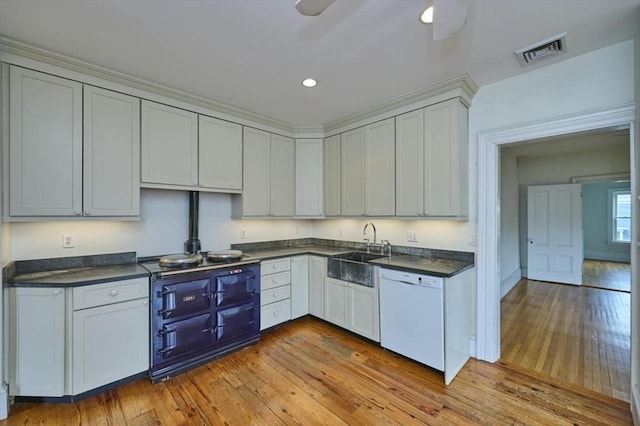 kitchen with white dishwasher, a sink, dark countertops, hardwood / wood-style flooring, and recessed lighting