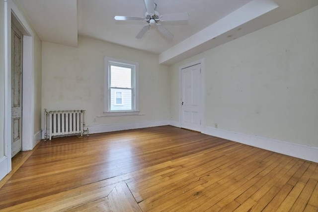 empty room with radiator, a ceiling fan, baseboards, and light wood-style flooring