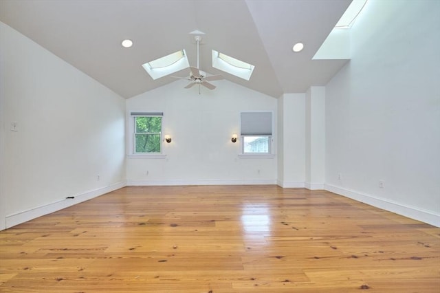 spare room featuring a skylight, light wood-style flooring, vaulted ceiling, and baseboards