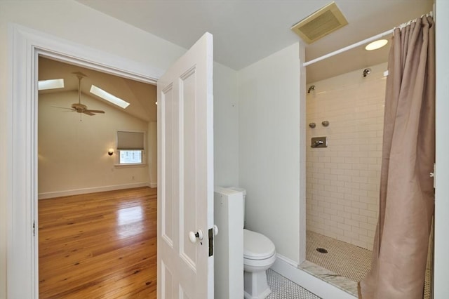 full bath with wood-type flooring, a tile shower, toilet, ceiling fan, and vaulted ceiling