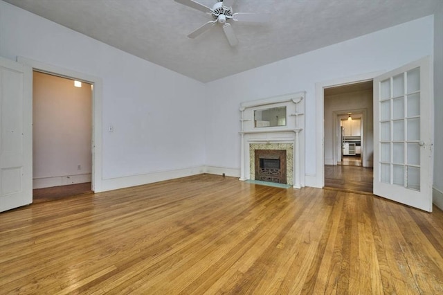unfurnished living room featuring a fireplace with flush hearth, ceiling fan, light wood-style floors, and built in features
