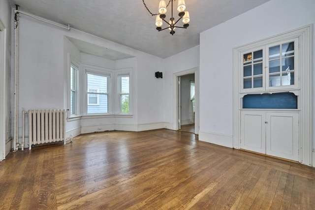 empty room with radiator, a chandelier, hardwood / wood-style floors, and baseboards