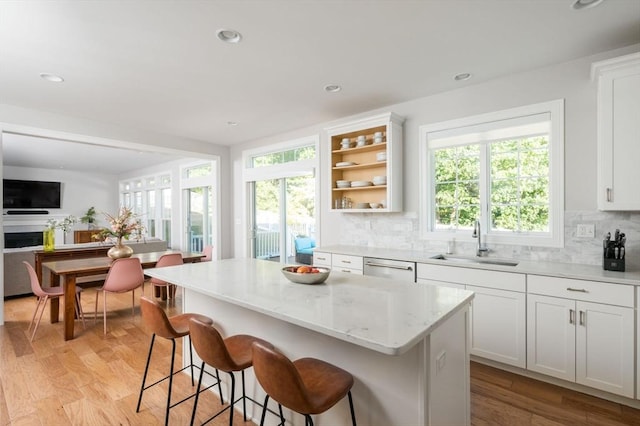 kitchen featuring light wood-style flooring, a sink, backsplash, a kitchen island, and a fireplace