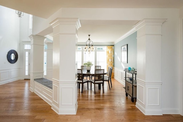 dining area featuring a decorative wall, light wood-style floors, a notable chandelier, and ornate columns