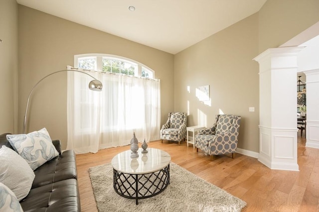 living area featuring decorative columns, lofted ceiling, and light wood finished floors