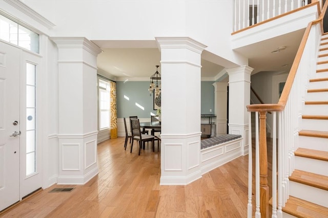 entryway featuring crown molding, a decorative wall, light wood finished floors, and ornate columns