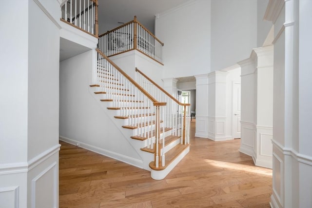 stairway featuring a decorative wall, ornamental molding, ornate columns, and wood finished floors