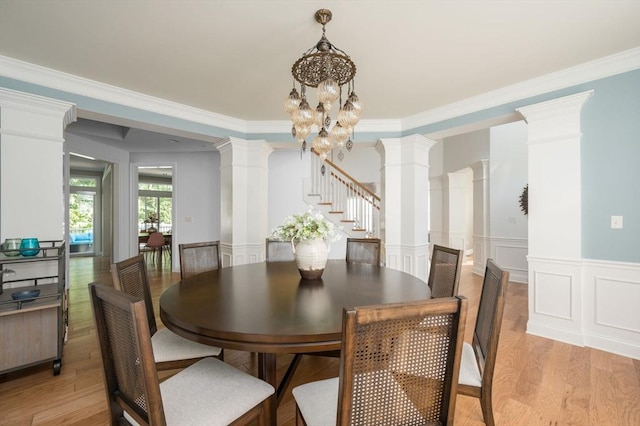 dining area featuring a wainscoted wall, light wood-style flooring, and ornate columns