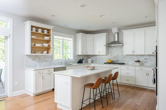 kitchen with gas cooktop, white cabinetry, light wood-type flooring, and wall chimney range hood