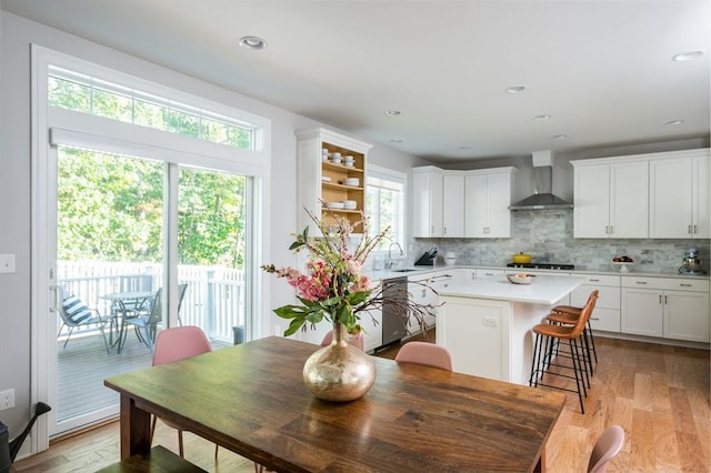 kitchen featuring a kitchen island, a sink, decorative backsplash, light countertops, and wall chimney range hood