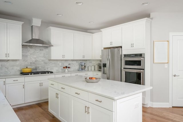 kitchen with wall chimney range hood, backsplash, white cabinetry, appliances with stainless steel finishes, and light wood finished floors