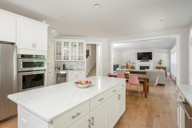 kitchen featuring white cabinetry, a fireplace, light wood-style floors, and stainless steel appliances