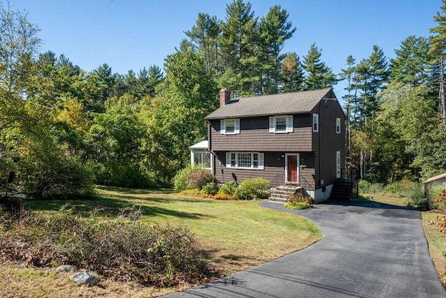 colonial house featuring a chimney, a front yard, and aphalt driveway