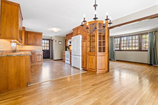 kitchen with brown cabinetry, a healthy amount of sunlight, white appliances, a chandelier, and a sink