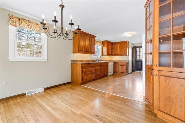 kitchen featuring visible vents, a chandelier, brown cabinets, dishwasher, and a wealth of natural light